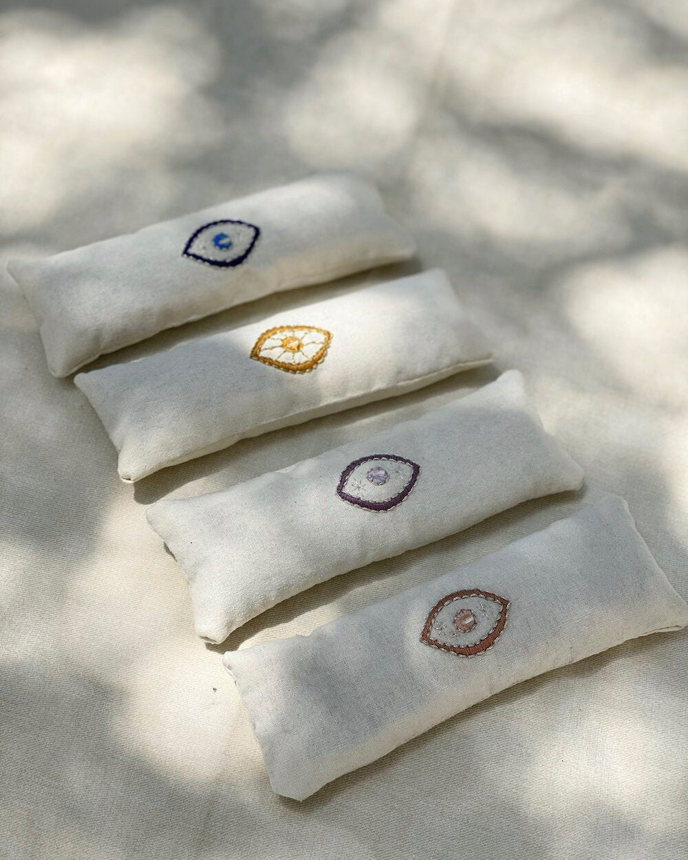 Five white pillows with embroidered designs on a light background