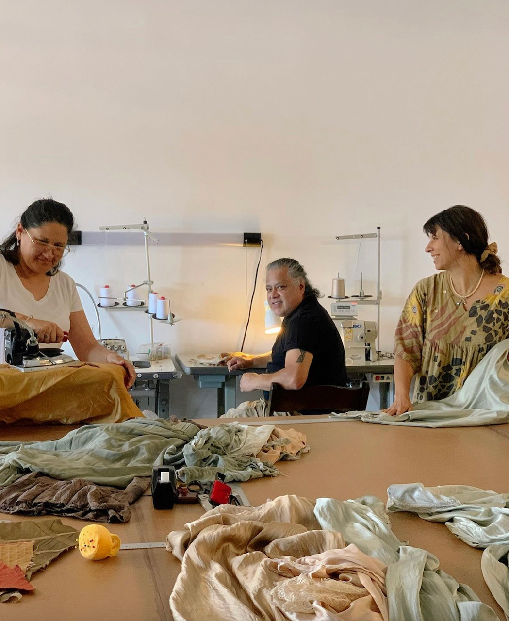Three people working together in a workshop with fabric and tools on a table.